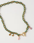 A gold-tone chain necklace with a green enamel inlay and small dangling charms, including a mauve heart, a pink coral charm, and a gold toggle clasp, displayed on a white background.