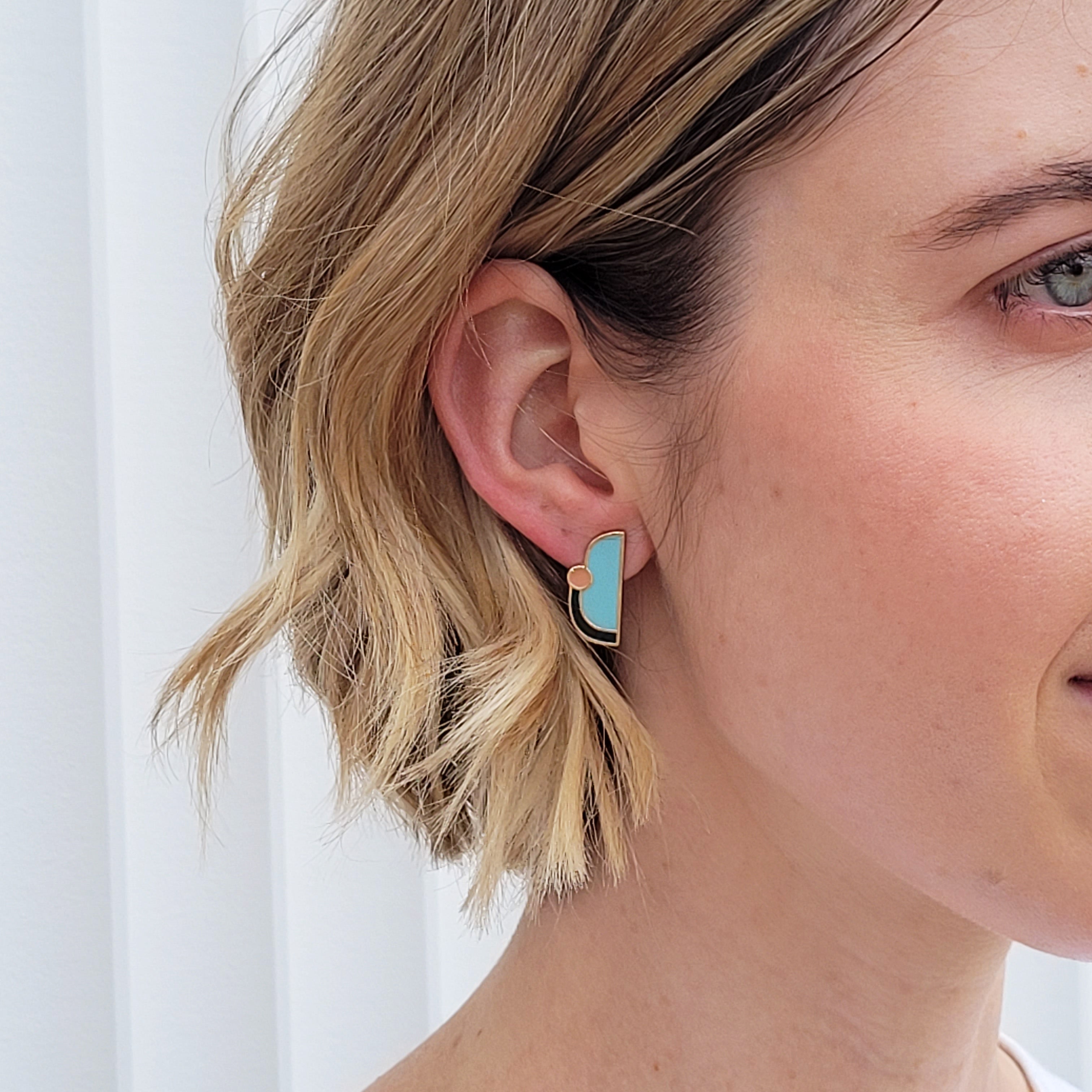A lady with short blonde hair models a close up, side view of the Division studs in ballet blue.