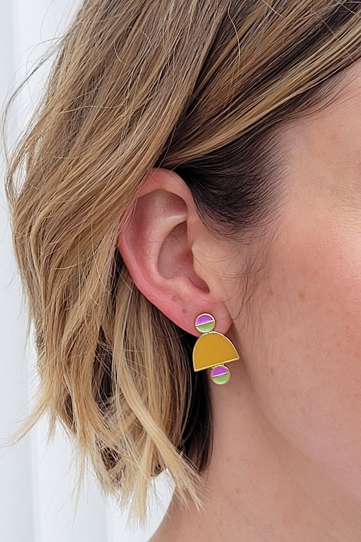 A lady with short blonde hair models a close up, side view of the Deuce studs in chartreuse.