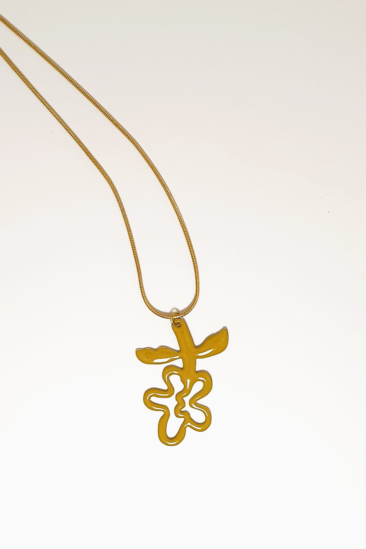 A necklace lays against a white background. It features a gold chain from which a chartreuse enamel abstract flower shape hangs upside down.