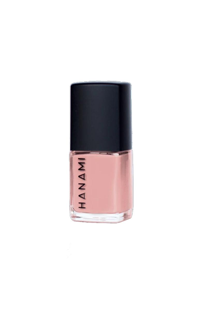 A bottle of nail polish in sits against a white background. It features a cubed glass bottle with the words HANAMI written in black uppercase text along one side and has a black cube-shaped lid. It is filled with a baby pink nail polish.