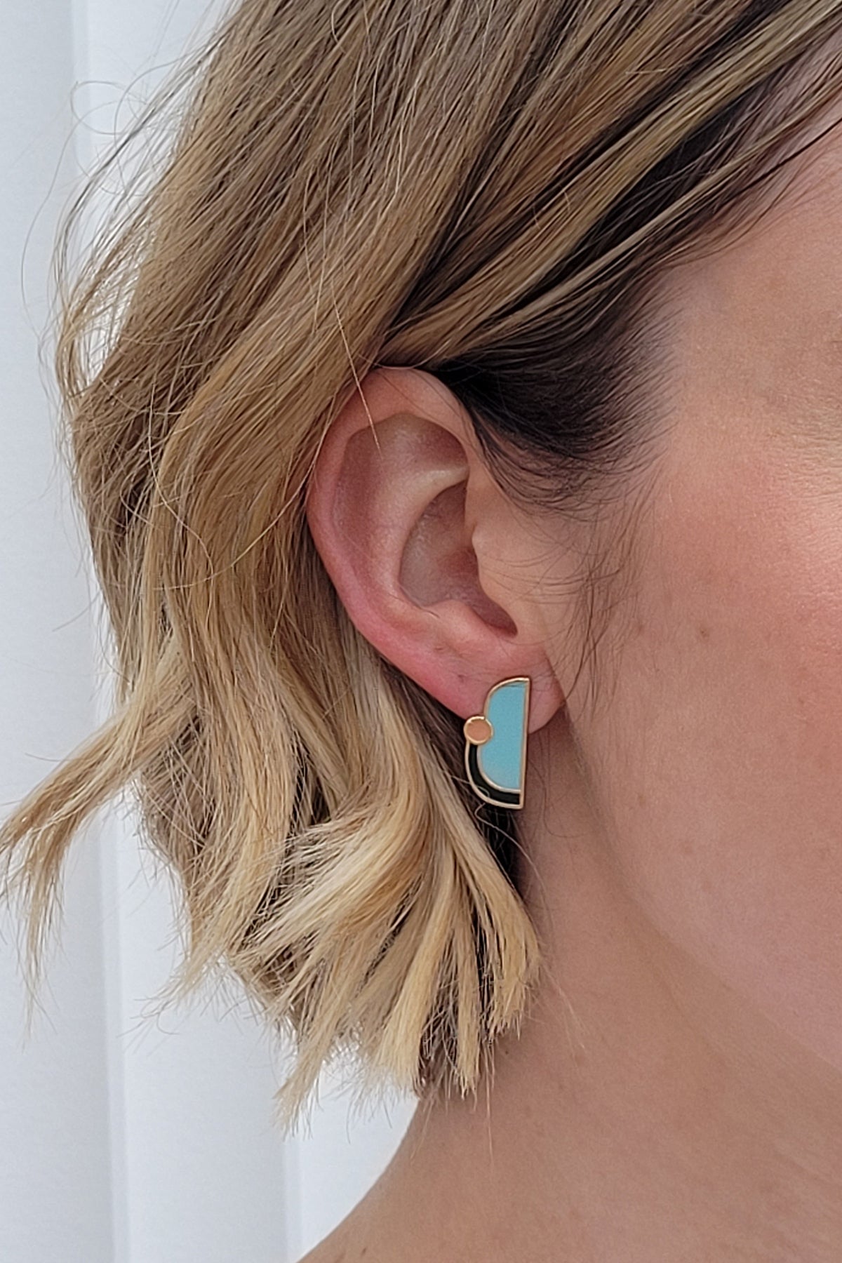 A lady with short blonde hair models a close up, side view of the Division studs in ballet blue.