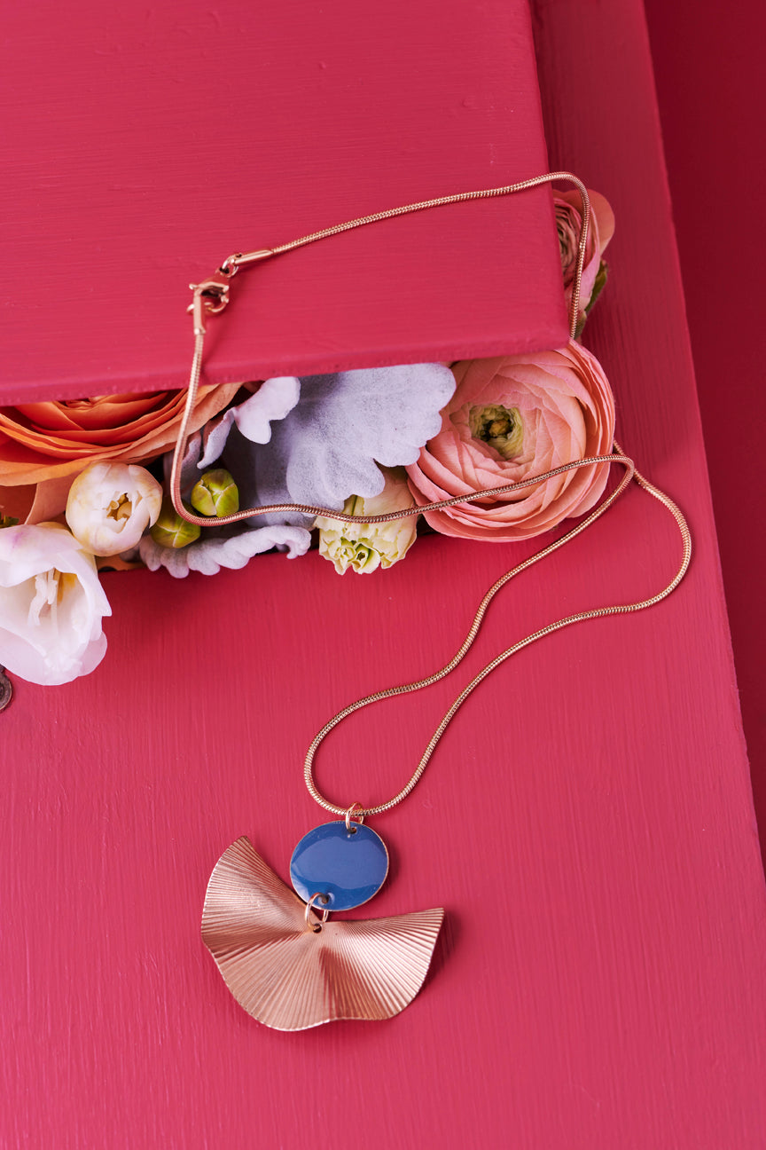 A Munroe necklace in Teal sits styled against a red background. A bouquet of flowers is placed nearby.