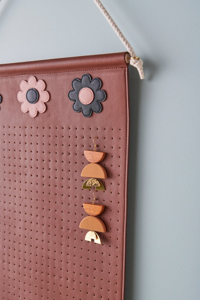 A close-up side view shows the perforated and floral details of the brown wall hanger, with a pair of mustard earrings displayed hanging from the holes.