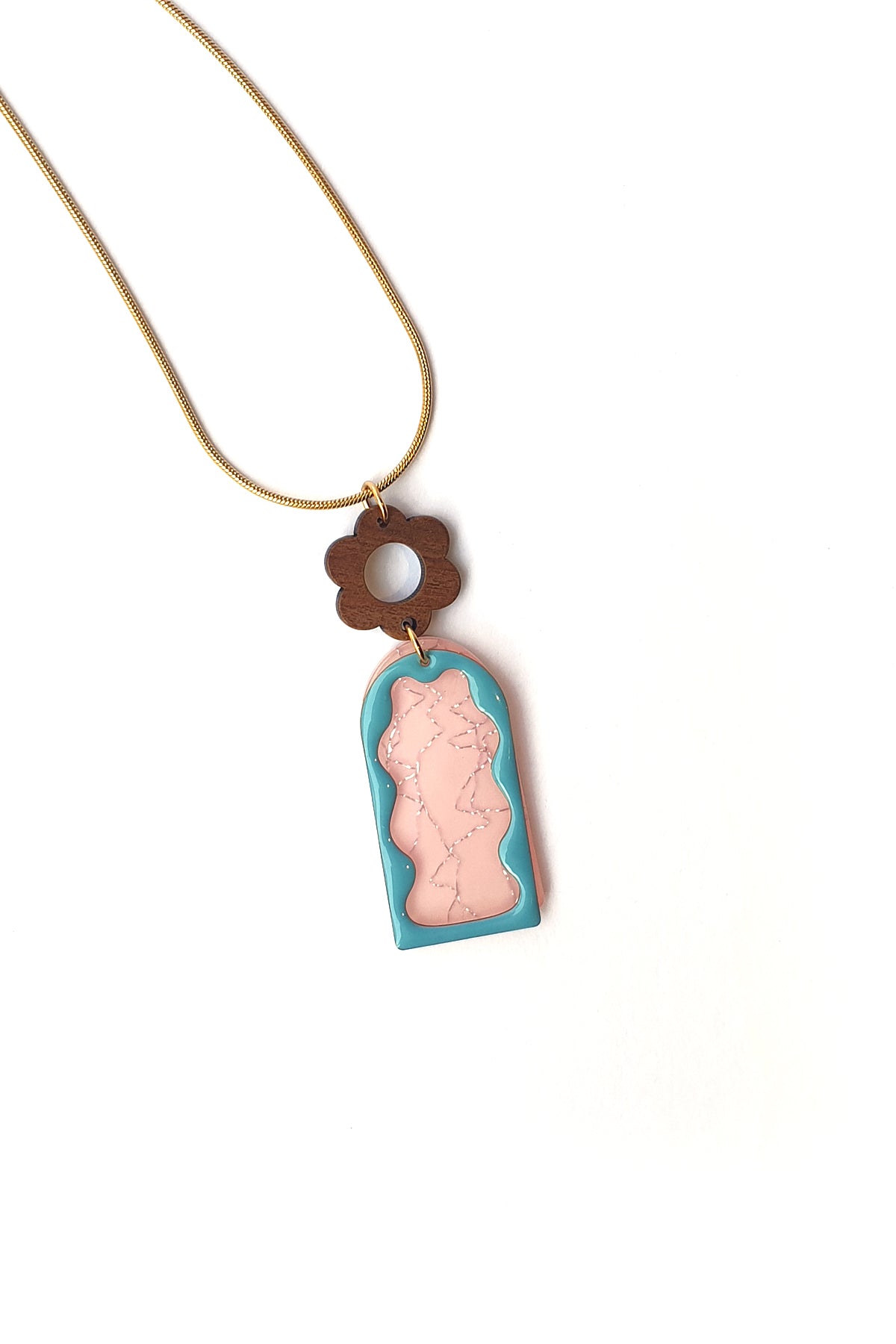 A necklace lays against a white background. It features a gold chain, a wooden flower top, followed by a pink acrylic arch with silver thread detail overlaid by a blue acrylic wavy arch frame.