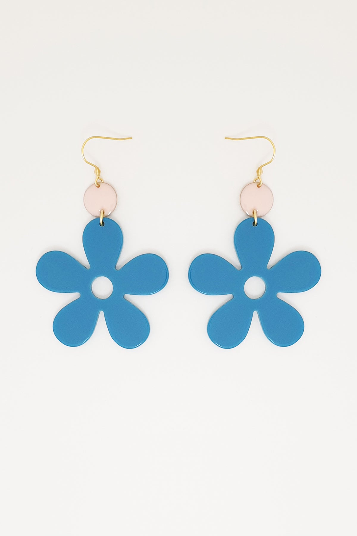 A pair of blue acrylic daisy dangle earrings with a light pink enamel dot attached to a hook. Pictured against a white background.