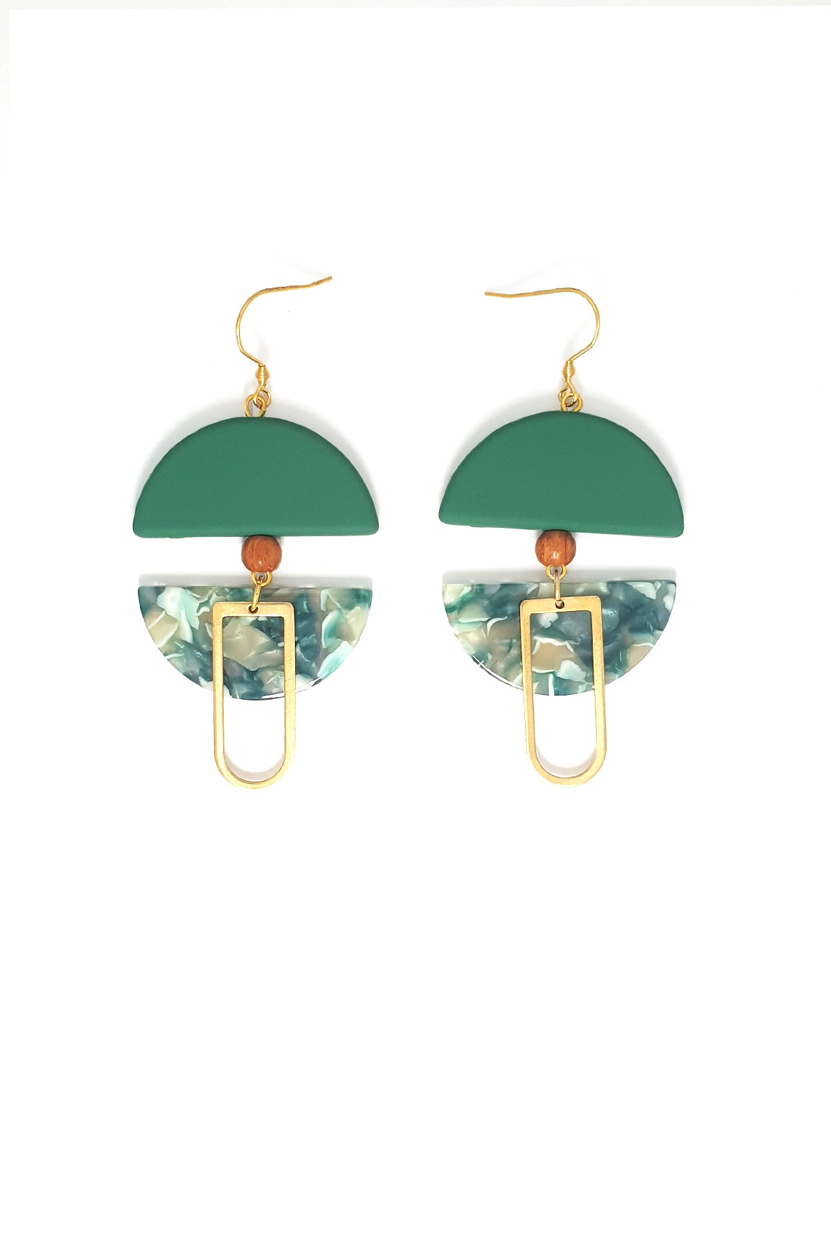 A pair of dangle earrings with a hook sit against a white background. They feature a green arch shaped bead, a small wooden bead, a green acrylic half circle, and an elongated D shape brass piece.