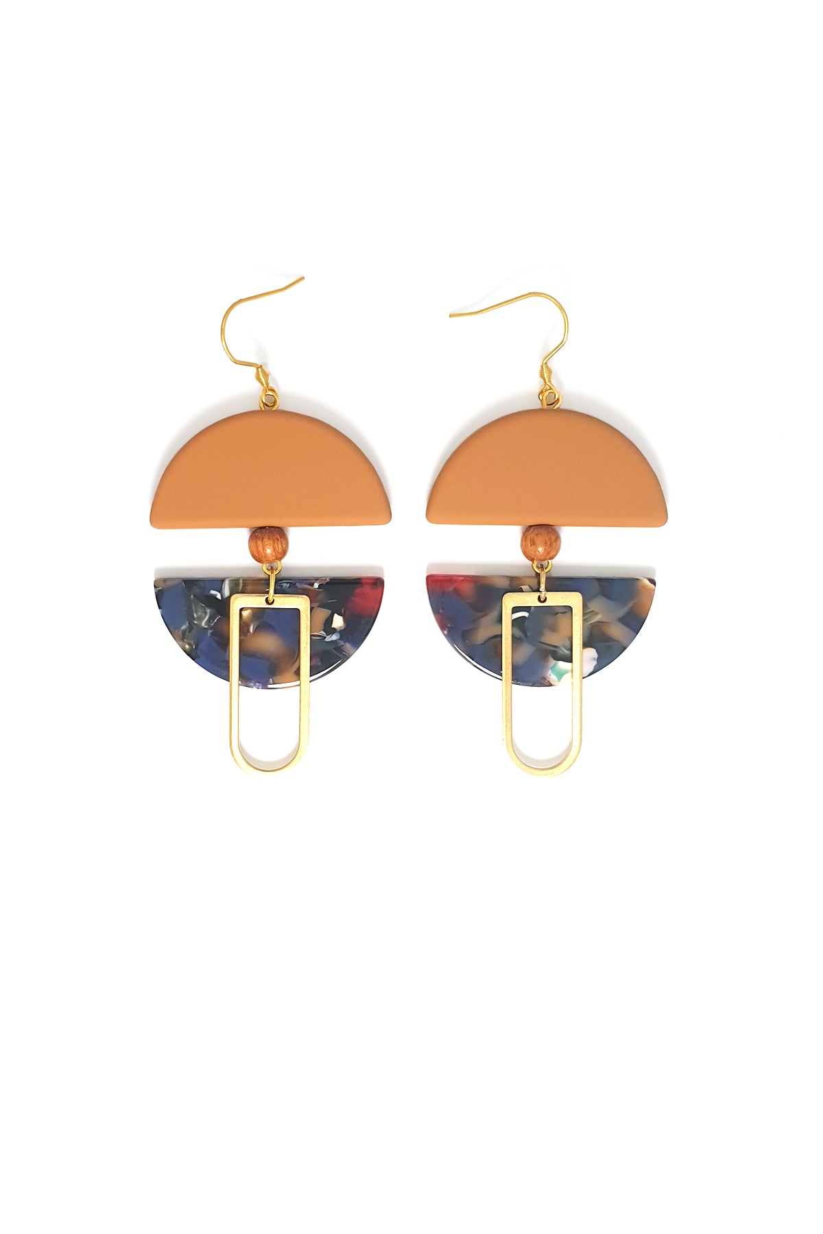 A pair of dangle earrings with a hook sit against a white background. They feature a mustard arch shaped bead, a small wooden bead, a blue and mustard acrylic half circle, and an elongated D shape brass piece.