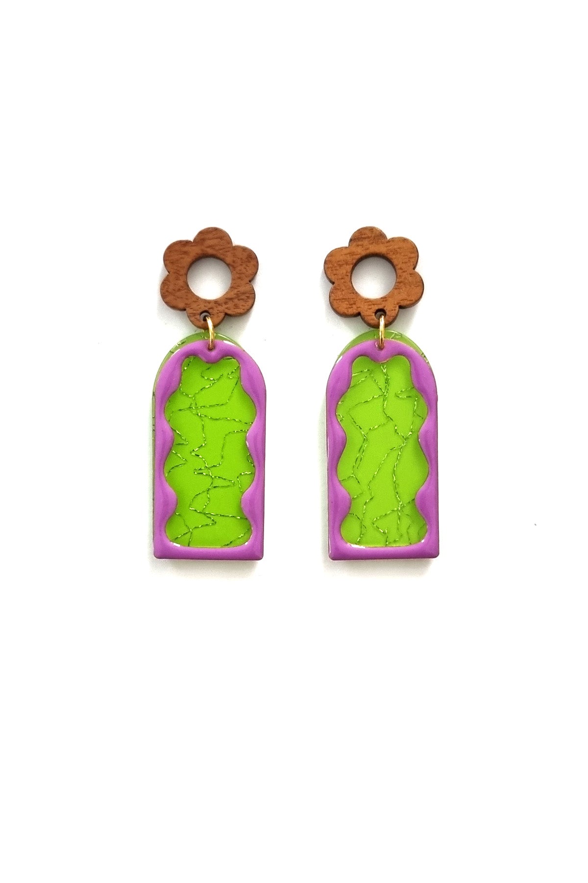 A pair of stud dangle earrings lay against a white background. They feature a wooden flower stud top followed by a green acrylic arch with a silver thread detail. On top sits an enamel wavy arch frame in purple.