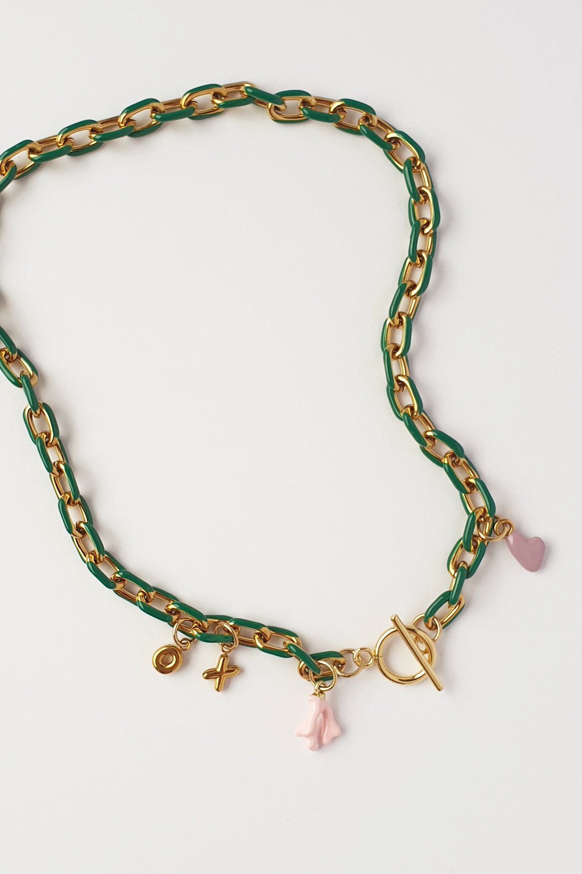 A gold-tone chain necklace with a green enamel inlay and small dangling charms, including a mauve heart, a pink coral charm, and a gold toggle clasp, displayed on a white background.
