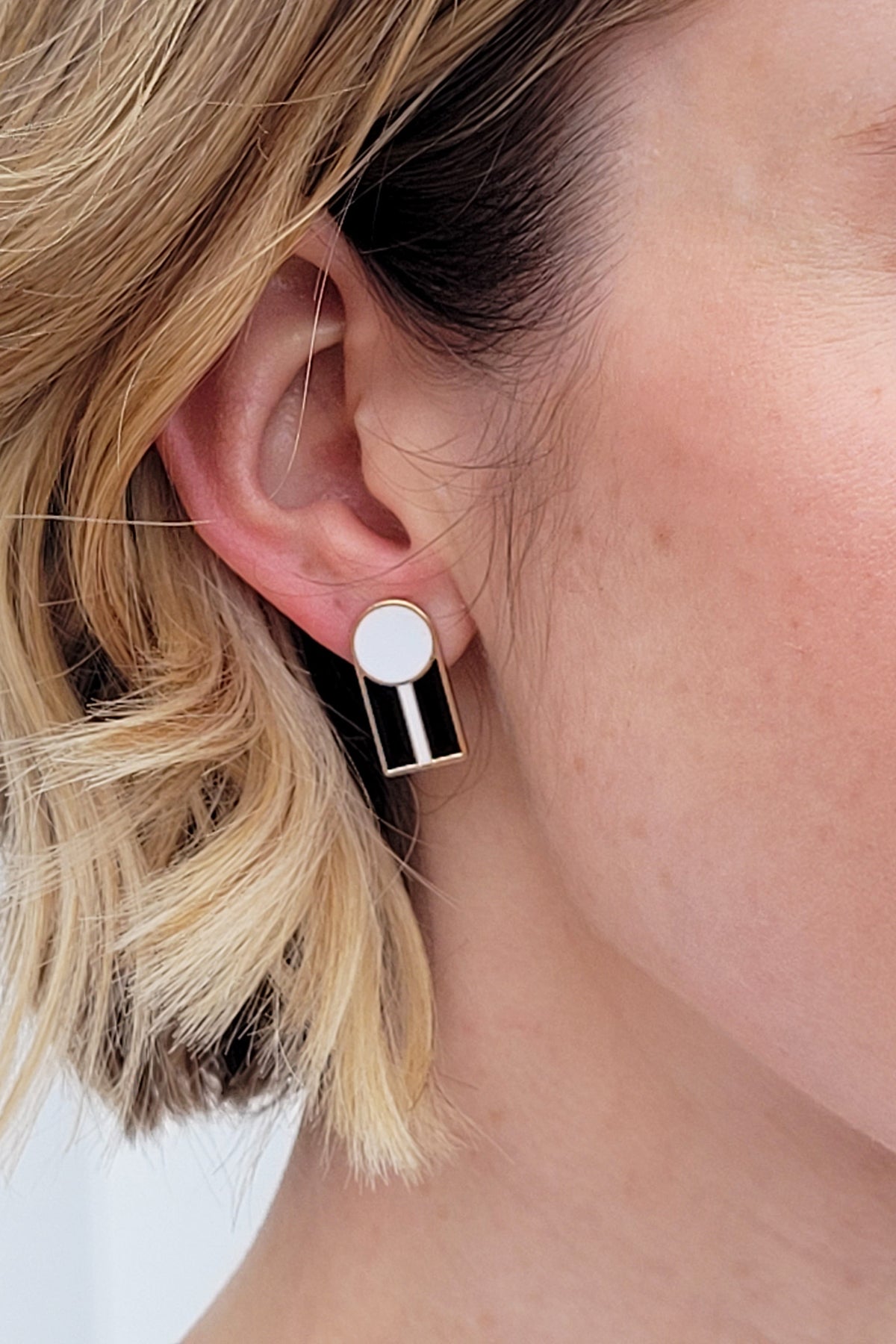 A close up of a lady with short blonde hair wearing a pair of the Graduate studs in the white with black colourway.