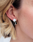 A close up of a lady with short blonde hair wearing a pair of the Graduate studs in the white with black colourway.