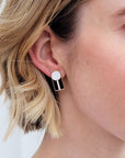 A close up of a lady with short blonde hair wearing a pair of the Graduate studs in the white with black colourway. 