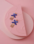 A pair of Lustre earrings in Sapphire sit styled against a background of foam blocks in different shades of pink.
