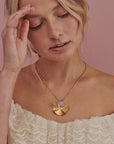 A lady with blonde hair models the Munroe necklace in mauve. She holds a hand up to her head and she wears a cream top with lace details.