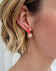A lady with blonde hair models a close up view of the Merit studs in red.