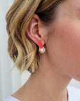 A lady with blonde hair models a close up view of the Merit studs in red.