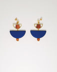  A pair of stud dangle earrings sit against a white background. They feature a small half circle brass piece with a wooden circle bead enclosed, below this hangs a blue D shape bead followed by a small wooden bead and a tiny gold bead.