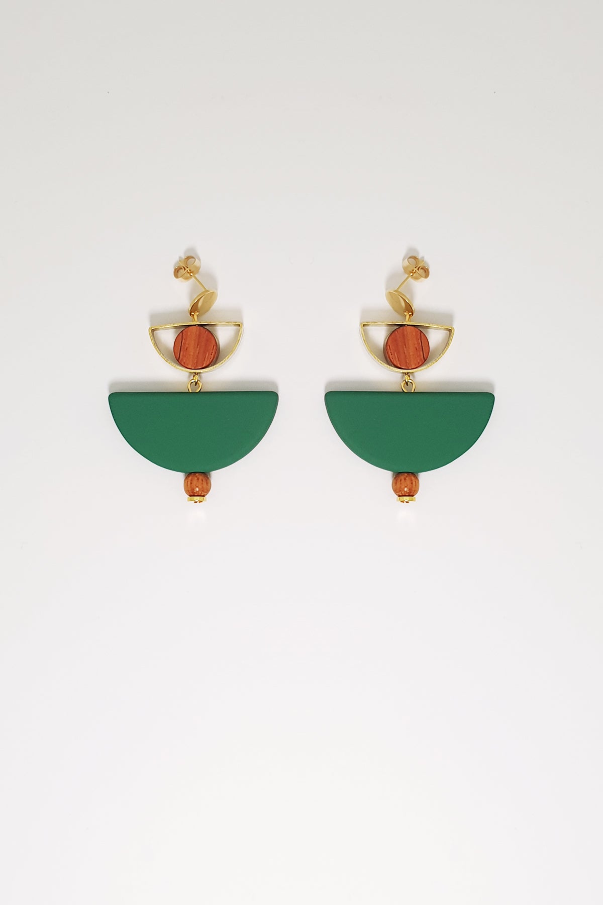 A pair of stud dangle earrings sit against a white background. They feature a small half circle brass piece with a wooden circle bead enclosed, below this hangs a green D shape bead followed by a small wooden bead and a tiny gold bead.