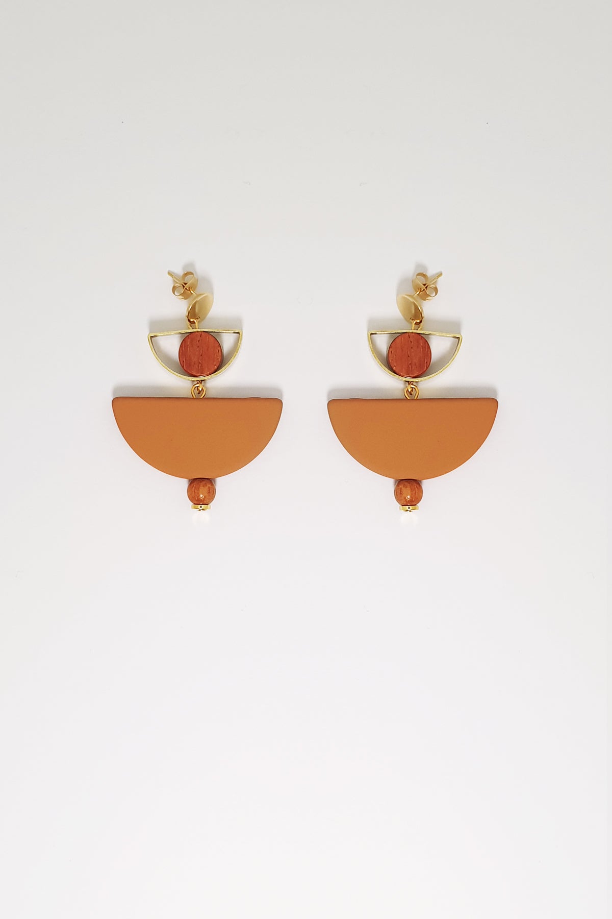 A pair of stud dangle earrings sit against a white background. They feature a small half circle brass piece with a wooden circle bead enclosed, below this hangs a mustard D shape bead followed by a small wooden bead and a tiny gold bead.