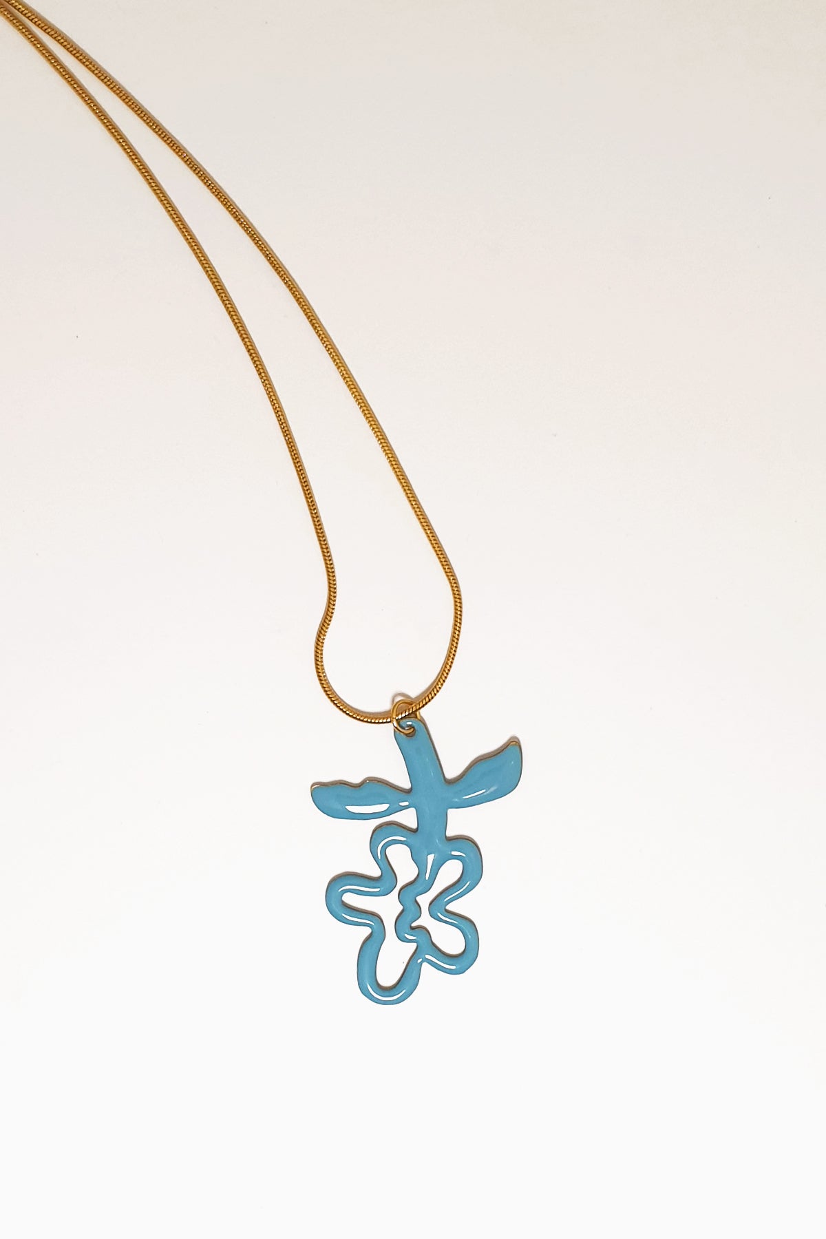 A necklace lays against a white background. It features a gold chain from which a blue enamel abstract flower shape hangs upside down.