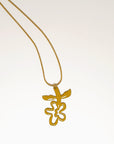A necklace lays against a white background. It features a gold chain from which a chartreuse enamel abstract flower shape hangs upside down.
