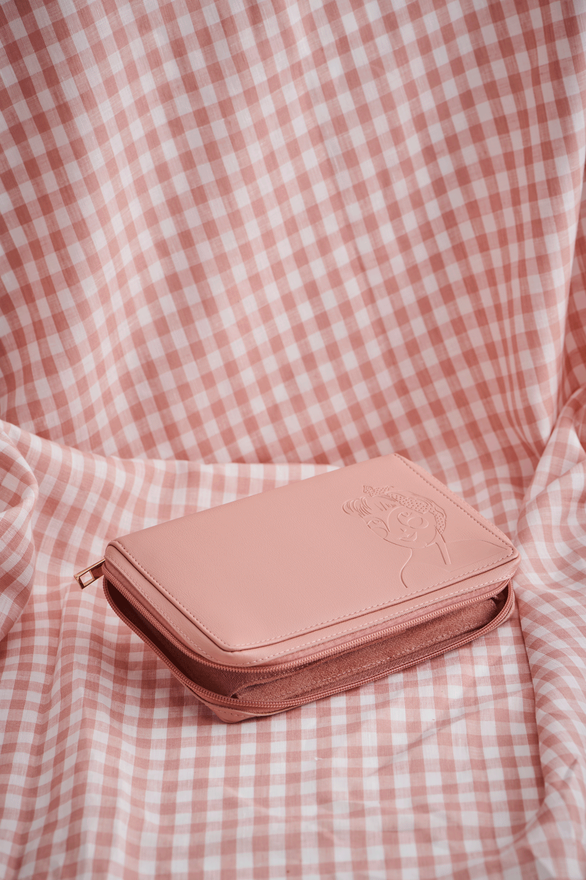 A moving image of a pink jewellery wallet on a pink check fabric background. It displays the functionality with the opening of the wallet, flaps and pockets and displays earrings and a necklace. The wallet then closes up again.
