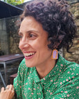 A lady with dark curly hair models a sideview of the Mixtape earrings in purple with orange frame. She sits outdoors and wears a green shirts with cream dots.