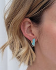 A lady with short blonde hair models a close up, side view of the Division studs in ballet blue.