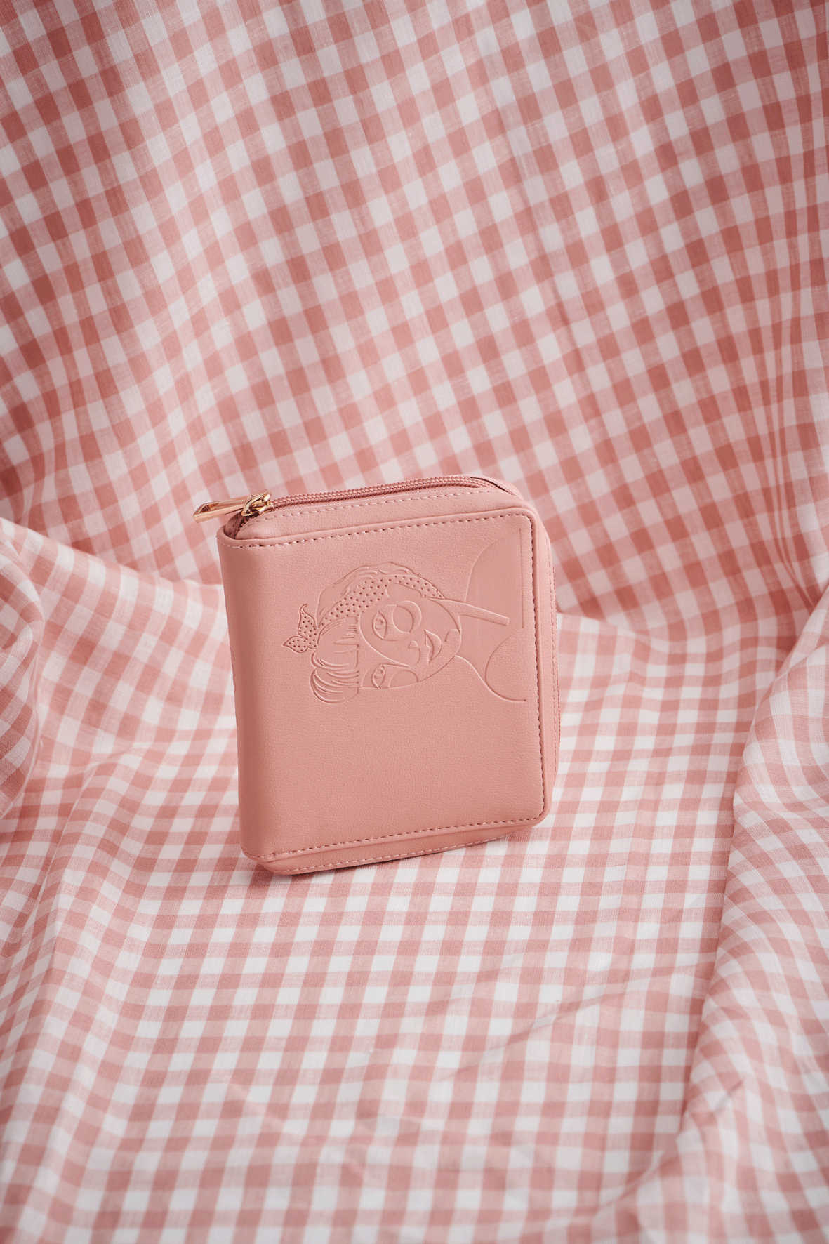 A moving image of a pink jewellery wallet on a pink check fabric background. It displays the functionality with the opening of the wallet, flaps and pockets and displays earrings and a necklace. The wallet then closes up again.