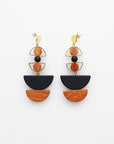 A pair of statement stud dangle earrings sit against a white background. They feature a small brass arch with a round wooden bead inside the arch, followed by a black bead, another small brass arch upturned with a wooden circle bead inside, followed by a black D shape bead, and wooden a D shape bead.