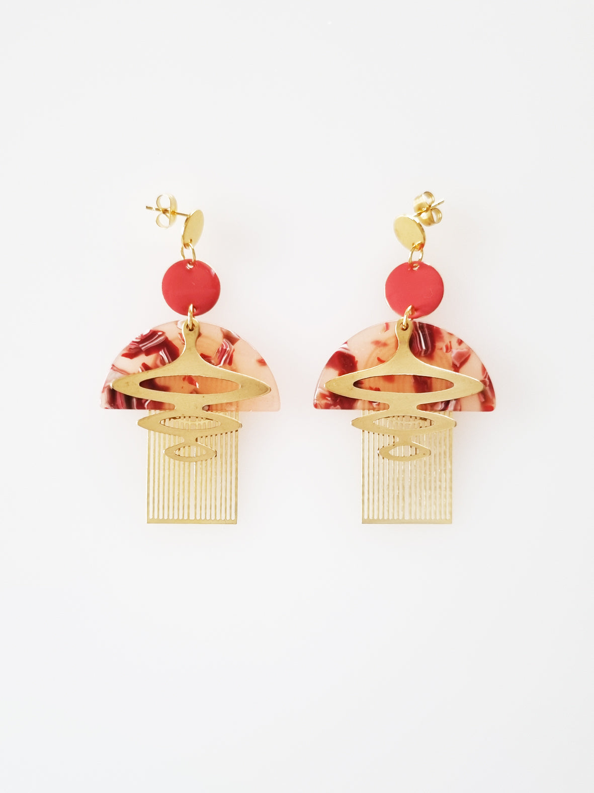 A pair of coral dangle earrings sits against a white background. The earrings feature a coral coloured enamel dot with a brass arch, coral acrylic half circle, and geometric brass pieces attached below.