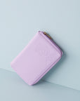A lilac jewellery wallet sits on an angle against a baby blue background. The wallet features an embossed image of a lady with a fringe and head scarf. It has a lilac zip and has a gold zip pull.