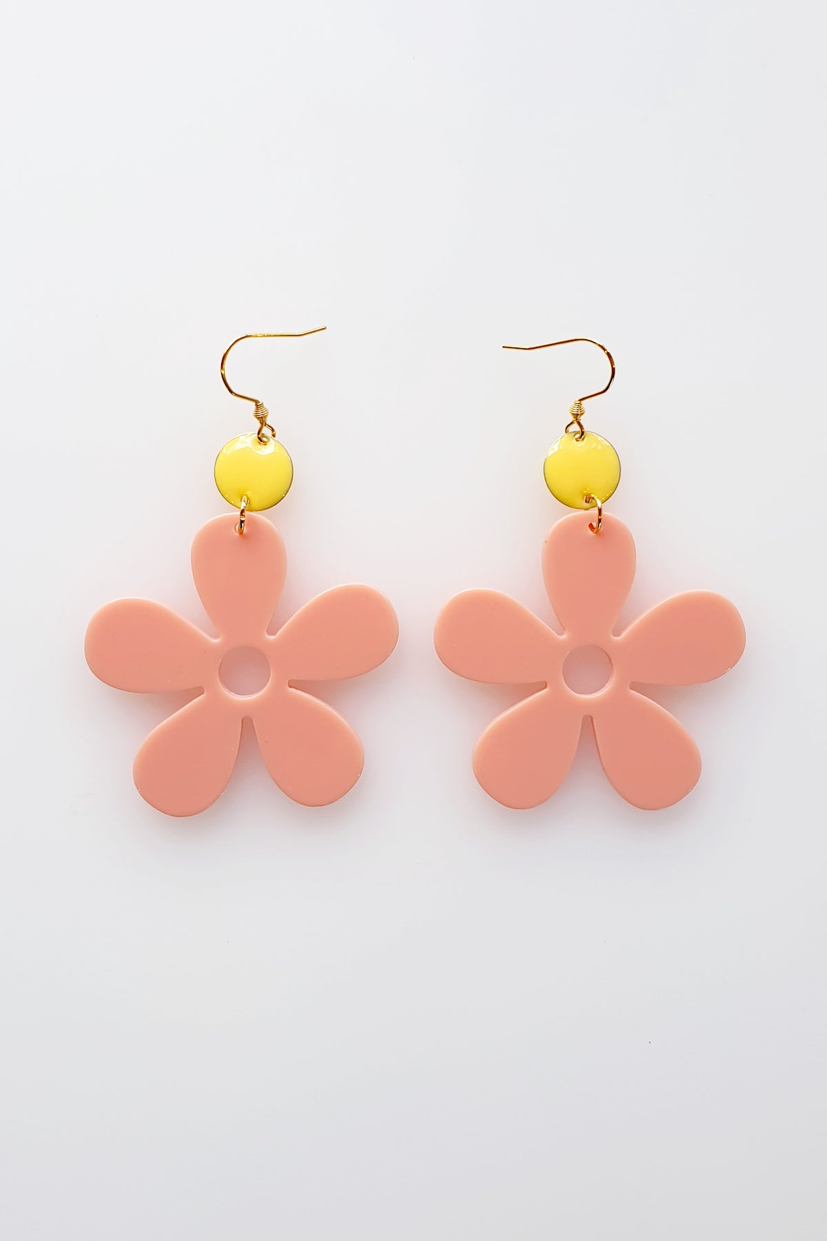 A pair of peach acrylic daisy dangle earrings with a lemon yellow enamel dot attached to a hook. Pictured flat against a white background.