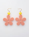 A pair of peach acrylic daisy dangle earrings with a lemon yellow enamel dot attached to a hook. Pictured flat against a white background.