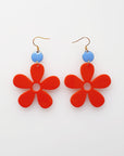 A pair of red acrylic daisy dangle earrings with a blue enamel dot attached to a hook. Pictured against a white background.
