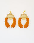 A pair of stud dangle earrings lay on a white background. Both earrings feature a semi circle piece of brass with scalloped detailing around the top curve. Behind that is a delicate circle piece of brass with thin lines cut vertically. A long mustard piece of enamel that has wavy edges is connected to the left of the brass semi-circle with a jump ring. A second enamel piece in the same shape is mirrored and connected to the right side of the brass semi-circle.