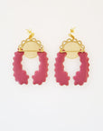 A pair of stud dangle earrings lay on a white background. Both earrings feature a semi circle piece of brass with scalloped detailing around the top curve. Behind that is a delicate circle piece of brass with thin lines cut vertically. A long plum piece of enamel that has wavy edges is connected to the left of the brass semi-circle with a jump ring. A second enamel piece in the same shape is mirrored and connected to the right side of the brass semi-circle.