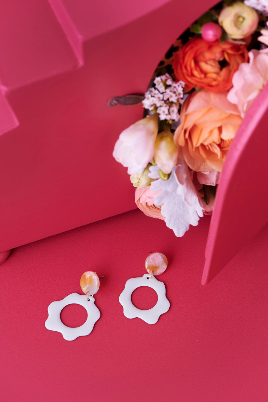The Floret earrings in honeydew sit styled against a cherry red background. A posy of flowerd are tucked under a cherry red stepped display.