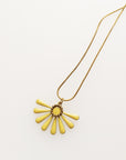 A necklace sits against a white background. It features a gold chain and a yellow coloured floral enamel shape. A tiny brass ring encircles the disk of the floral enamel piece.
