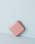 A pink jewellery wallet sits on an angle against a baby blue background. The wallet features an embossed image of a lady with a fringe and head scarf. It has a pink zip and has a gold zip pull.