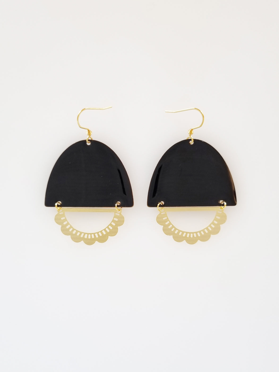 A pair of statement earrings with a hook sit against a white background. They feature a black enamel arch and a horizontal plated brass D shape with scalloped detail.