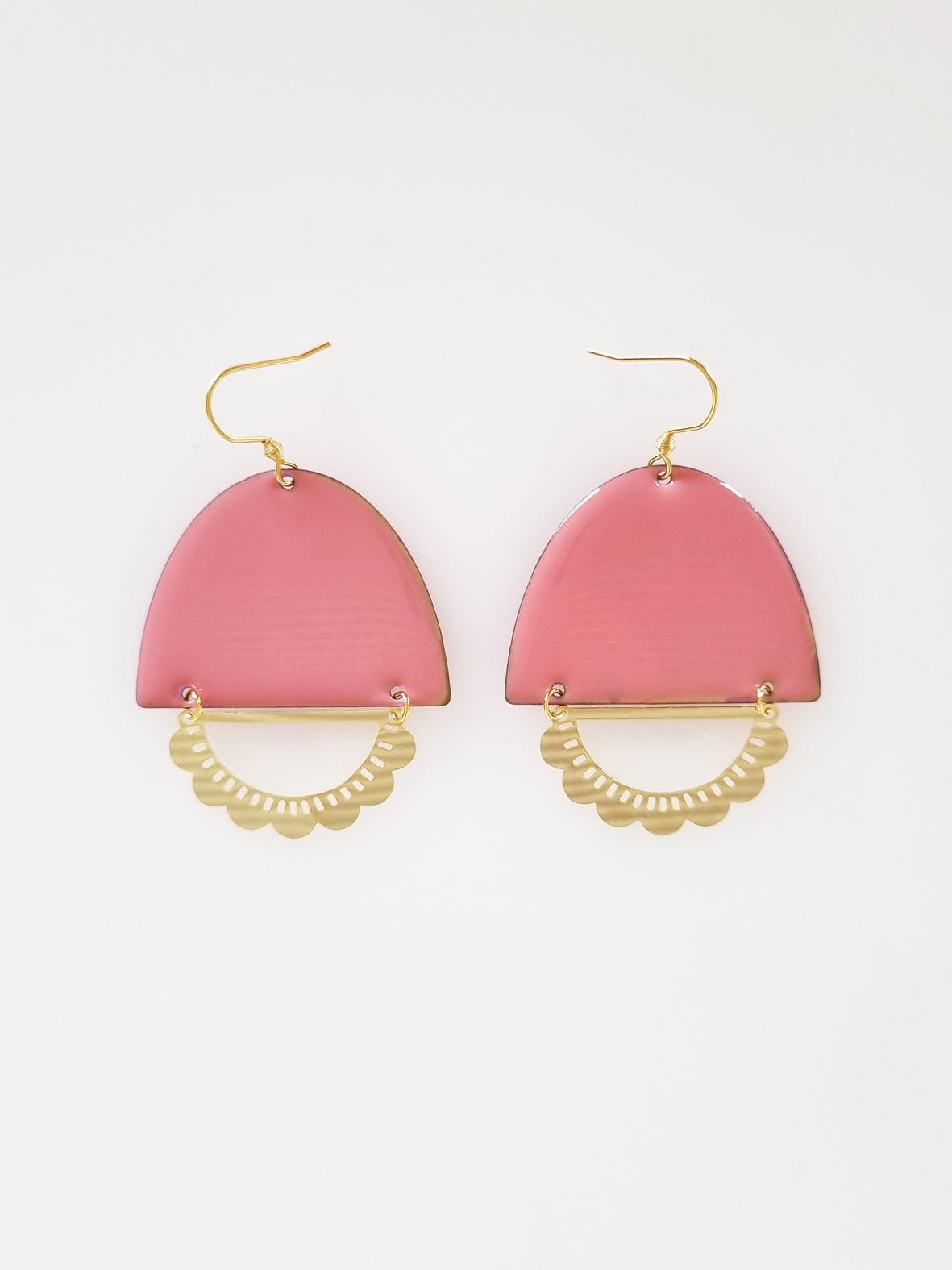 A pair of statement earrings with a hook sit against a white background. They feature a pink enamel arch and a horizontal plated brass D shape with scalloped detail.