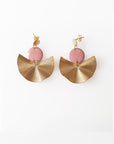 A pair of stud dangle earrings sit against a white background.  They feature a pink enamel connector dot and a textured brass fan piece.