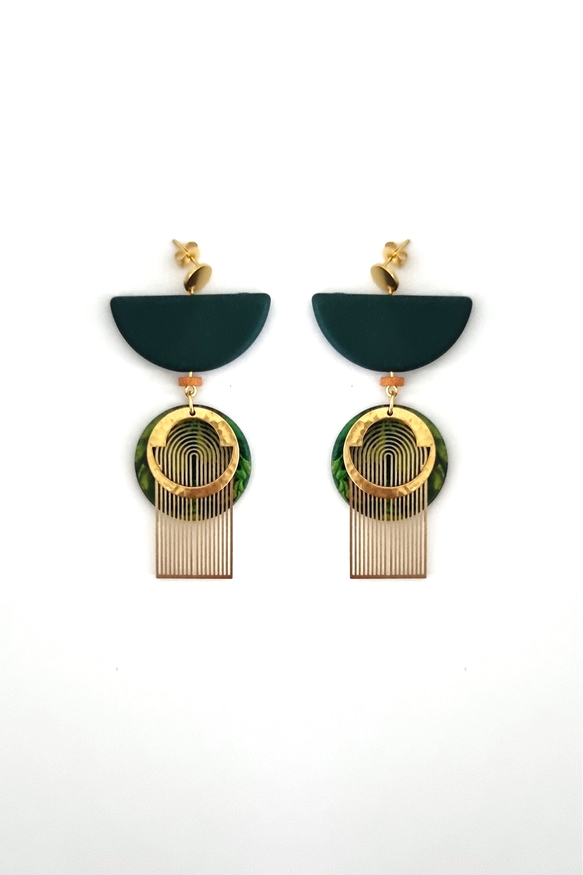 A pair of green dangle earrings with a stud top sit against a white background. They feature a green half circle bead, a small wooden bead, a green acrylic circle, a brass arch piece, and a textured circular brass piece.
