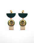 A pair of green dangle earrings with a stud top sit against a white background. They feature a green half circle bead, a small wooden bead, a green acrylic circle, a brass arch piece, and a textured circular brass piece.