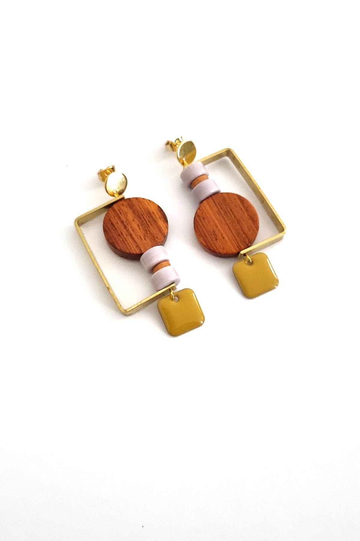 A pair of stud dangle earrings lay against a white background. They feature a half square brass shape that envelopes a circular wooden bead, and two mauve stone beads separated by a small wooden bead. The design is flipped in each ear and a chartreuse square enamel dangle hangs from the bottom on each earring.