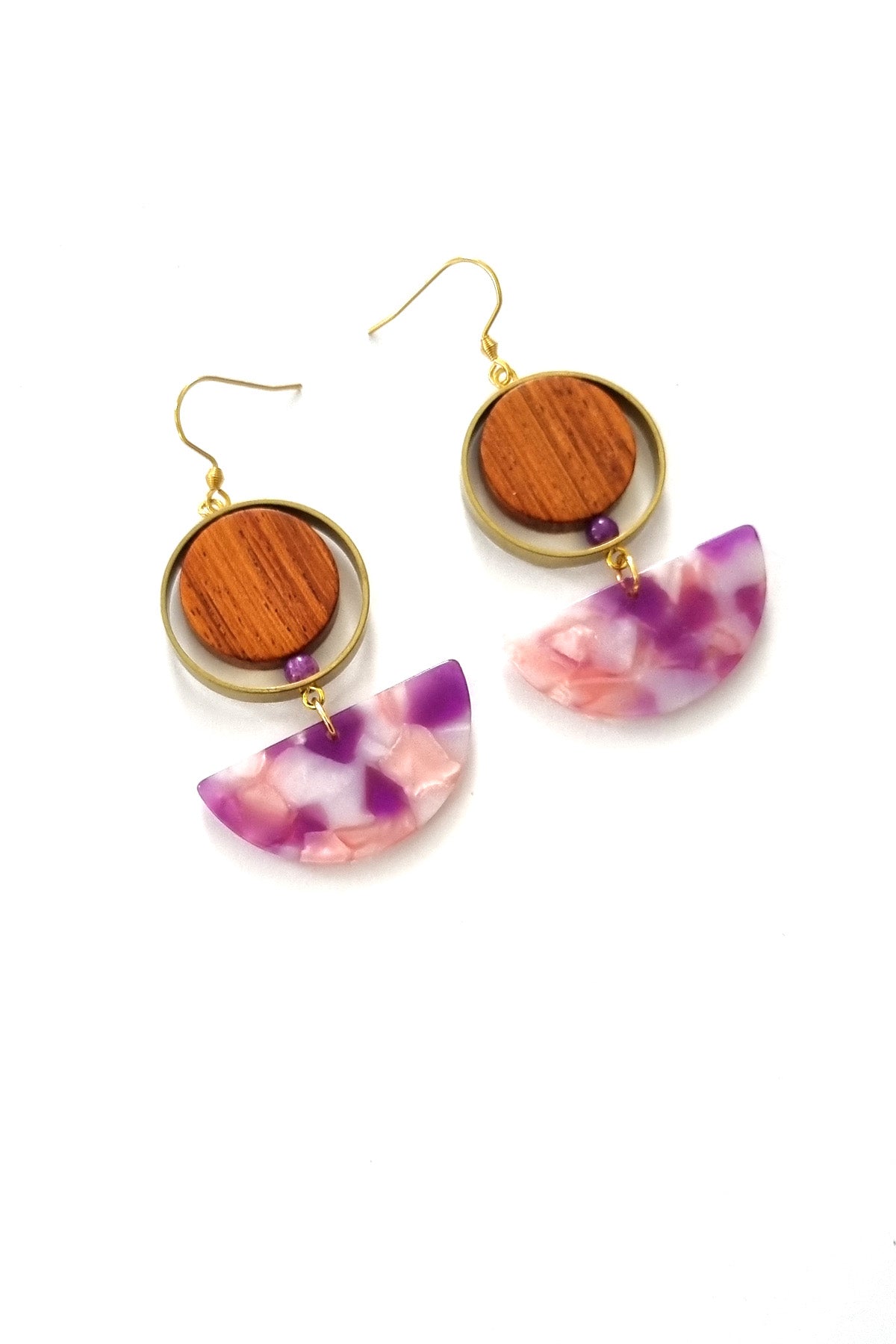 A pair of hook dangle earrings sit against a white background. They feature a circular wooden bead and a small purple bead encircled by a brass ring. Below dangles a pink and purple multicoloured D-shaped acrylic piece.