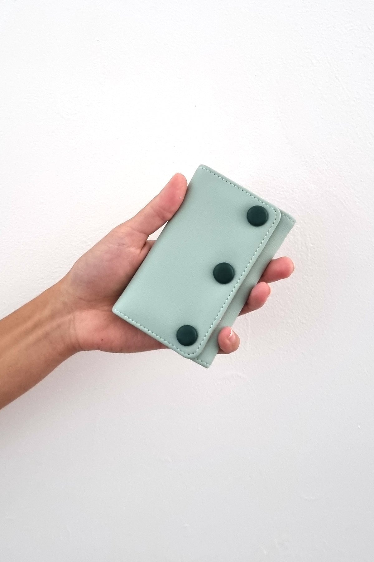 An outstretched hand holds a duckegg jewellery snug against a white wall. The snug features duckegg PU and has three PU covered buttons in teal.