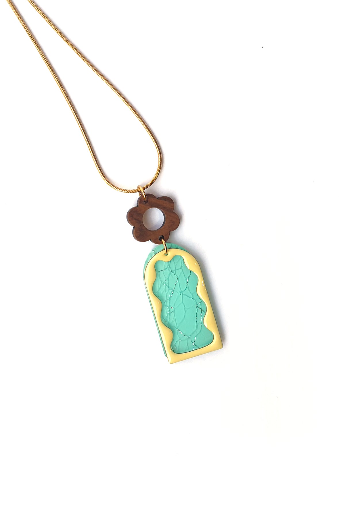 A necklace lays against a white background. It features a gold chain, a wooden flower top, followed by a aqua acrylic arch with silver thread detail overlaid by a yellow acrylic wavy arch frame.